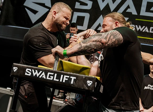 Two men in a&nbsp;tense armwrestling battle in front of a&nbsp;SWAGLIFT DAY banner